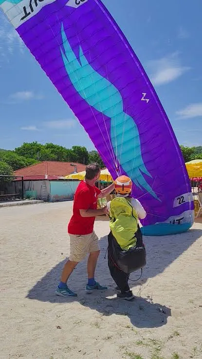 Instructor steadying a student under a purple parakite wing on the sand