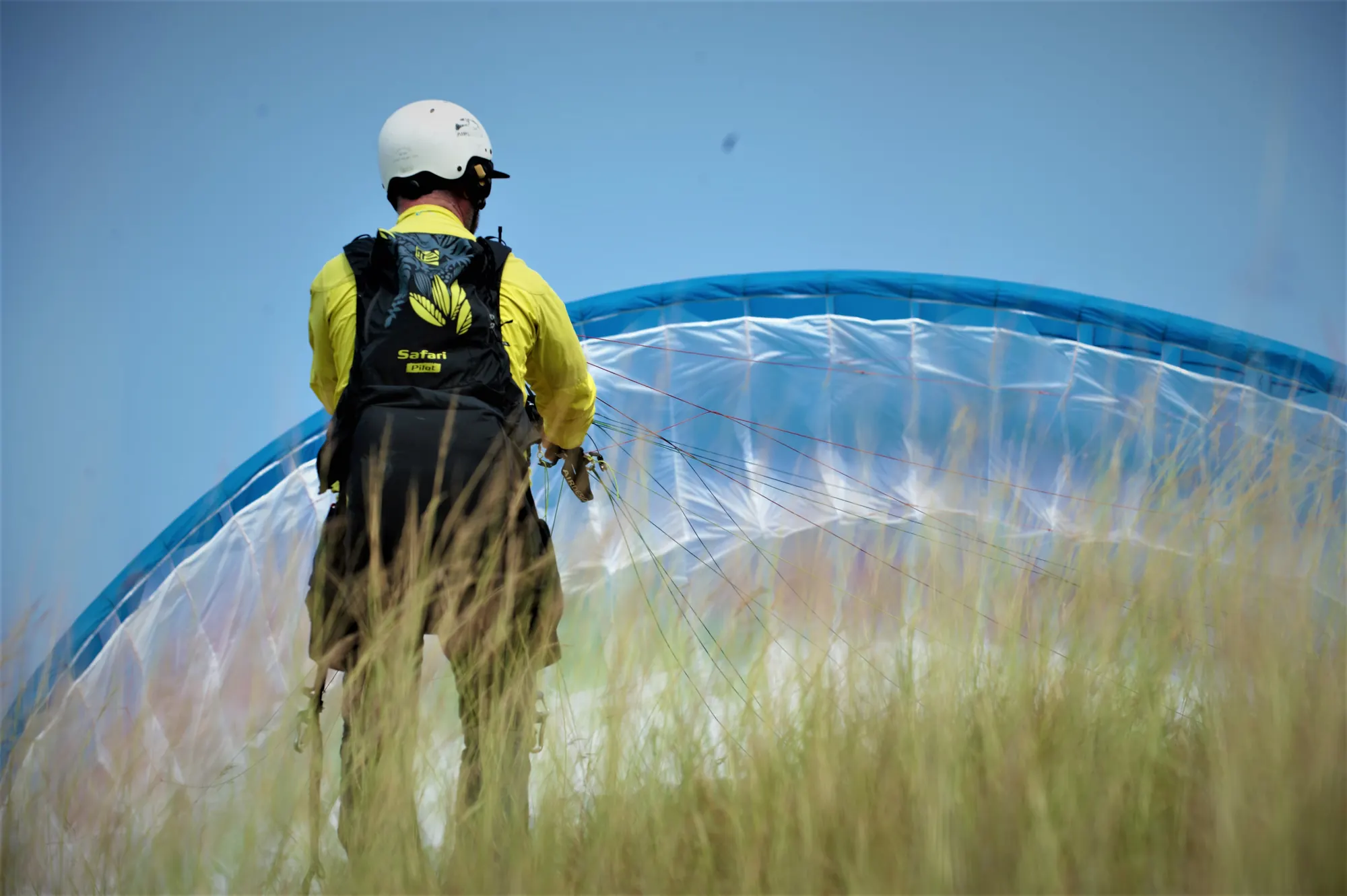 Student pilot in a helmet ground handling a blue and white paraglider in long grass