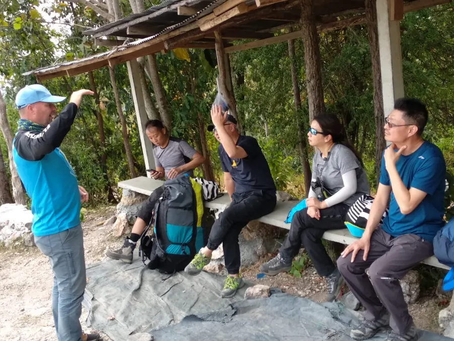 Guide giving a site briefing to a group of visiting pilots under a shelter at take-off