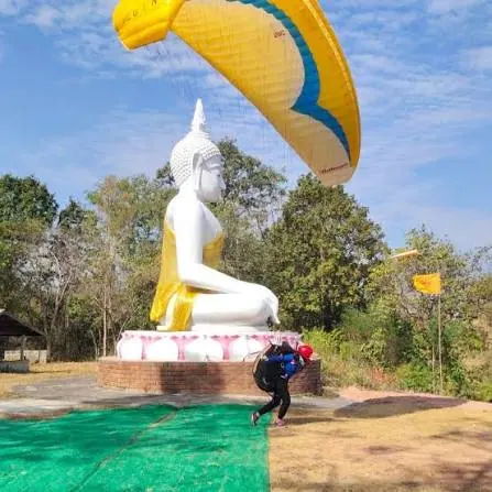 Pilot launching a yellow wing beside a large white Buddha statue